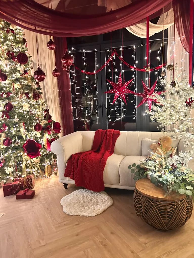 Kremowa sofa, czerwony koc, piernikowy miś i czerwone gwiazdy nad oknem