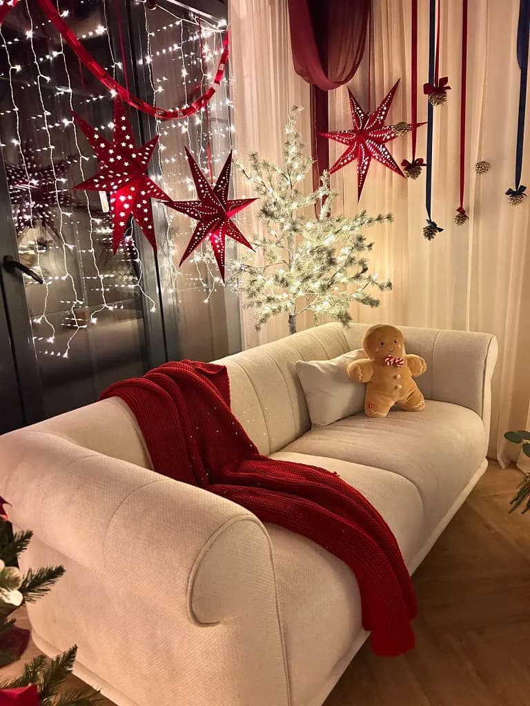 Sofa z czerwonym kocem i pluszowym piernikiem przy oknie z lampkami